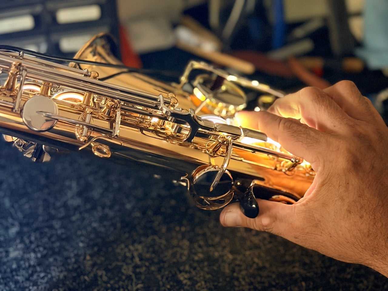 A close-up of a person’s hand pressing the keys of a shiny gold saxophone, with soft lighting highlighting the instrument’s details and a blurred background.