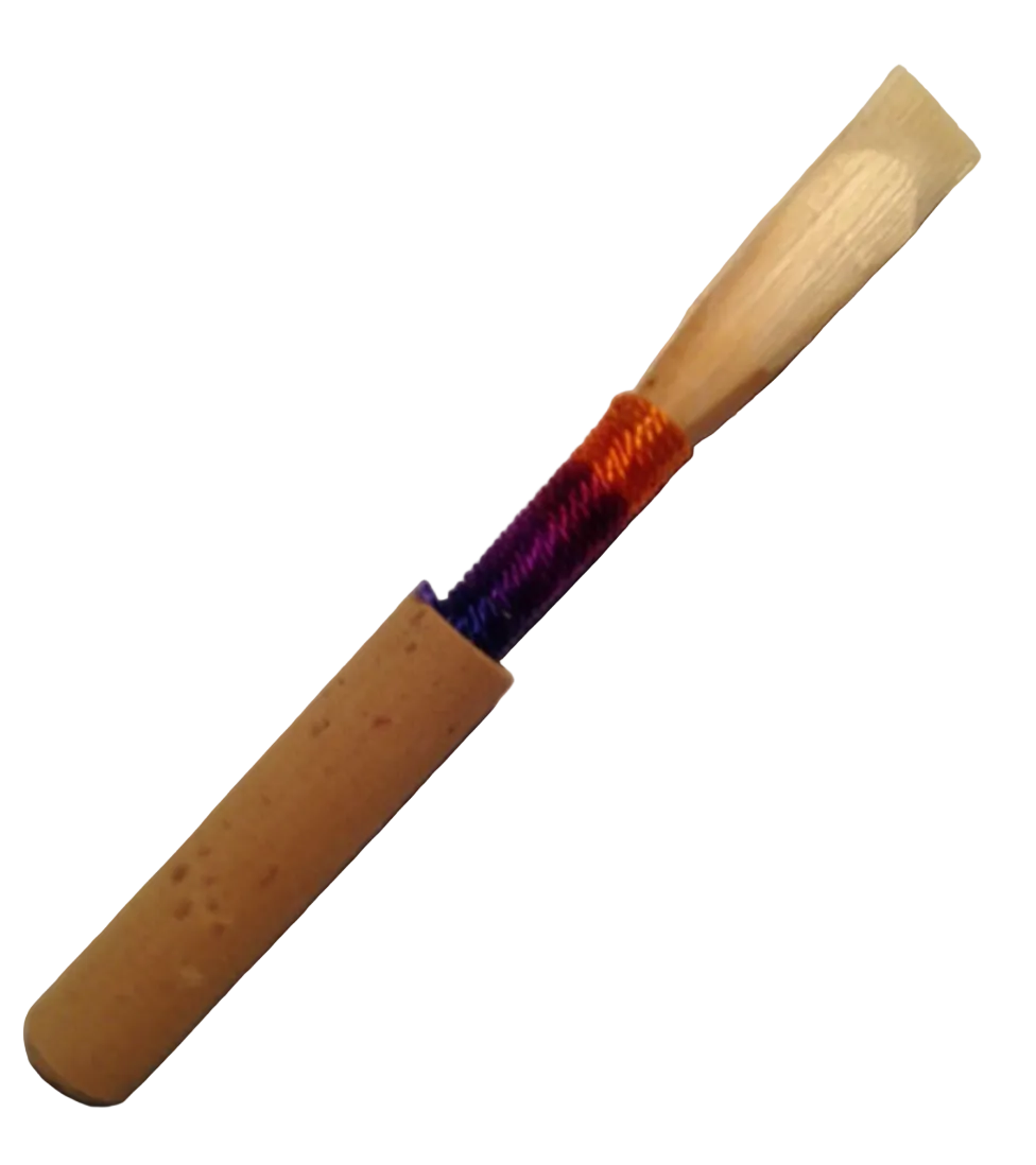 A Singin' Dog Oboe Reed with a light wooden blade, cork base, and purple-to-orange gradient thread rests on a white surface—a stylish, handmade choice for double reed musicians or oboe reed enthusiasts.