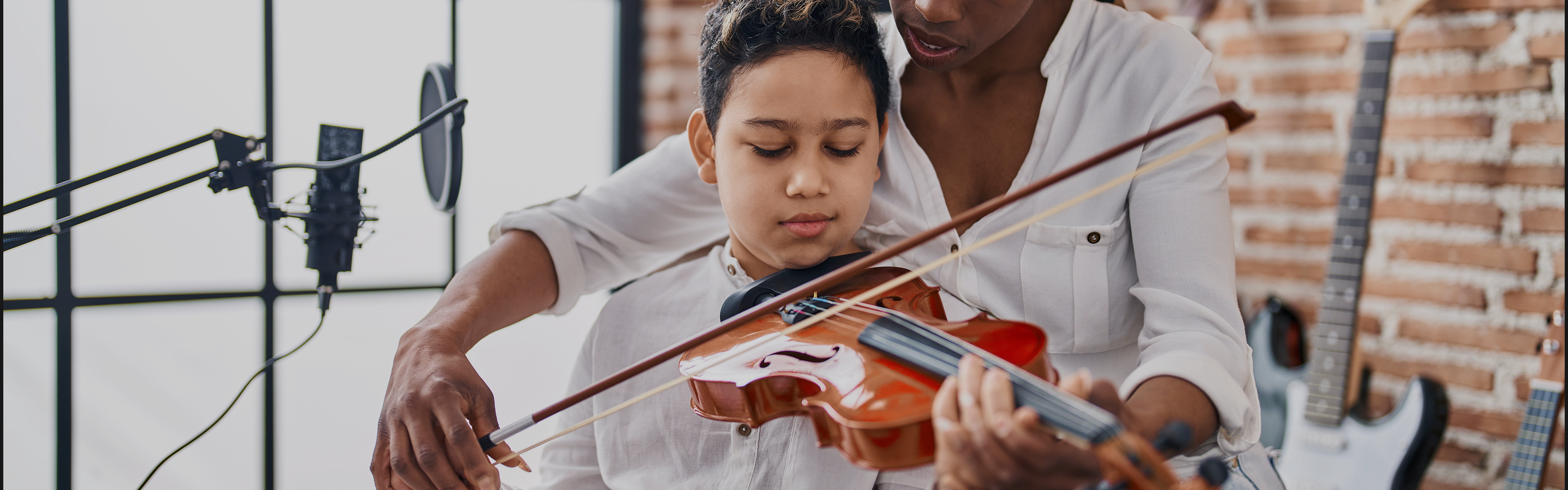 Young boy learning violin with teacher behind him guiding the violin bow