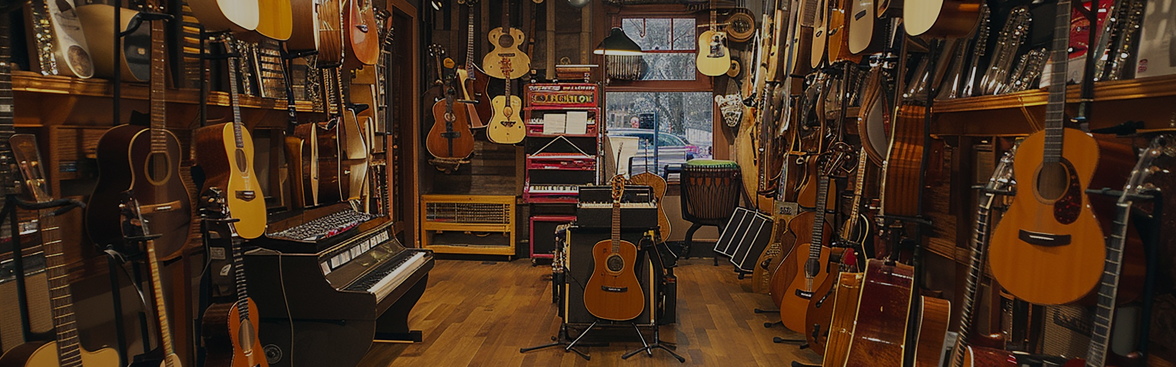 A cozy music store lined with acoustic and electric guitars on the walls, keyboards, and various percussion instruments, including a drum and bongos, displayed on shelves and stands. Warm lighting highlights the wooden floor.